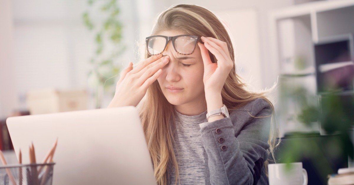 young woman rubbing eyes sitting at desk in front of computer