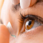 A female inserting a contact lens into her left eye.