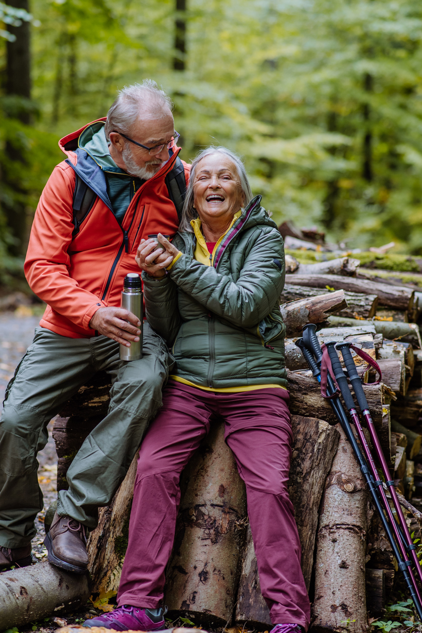 Senior couple having break during hiking in autumn forest.